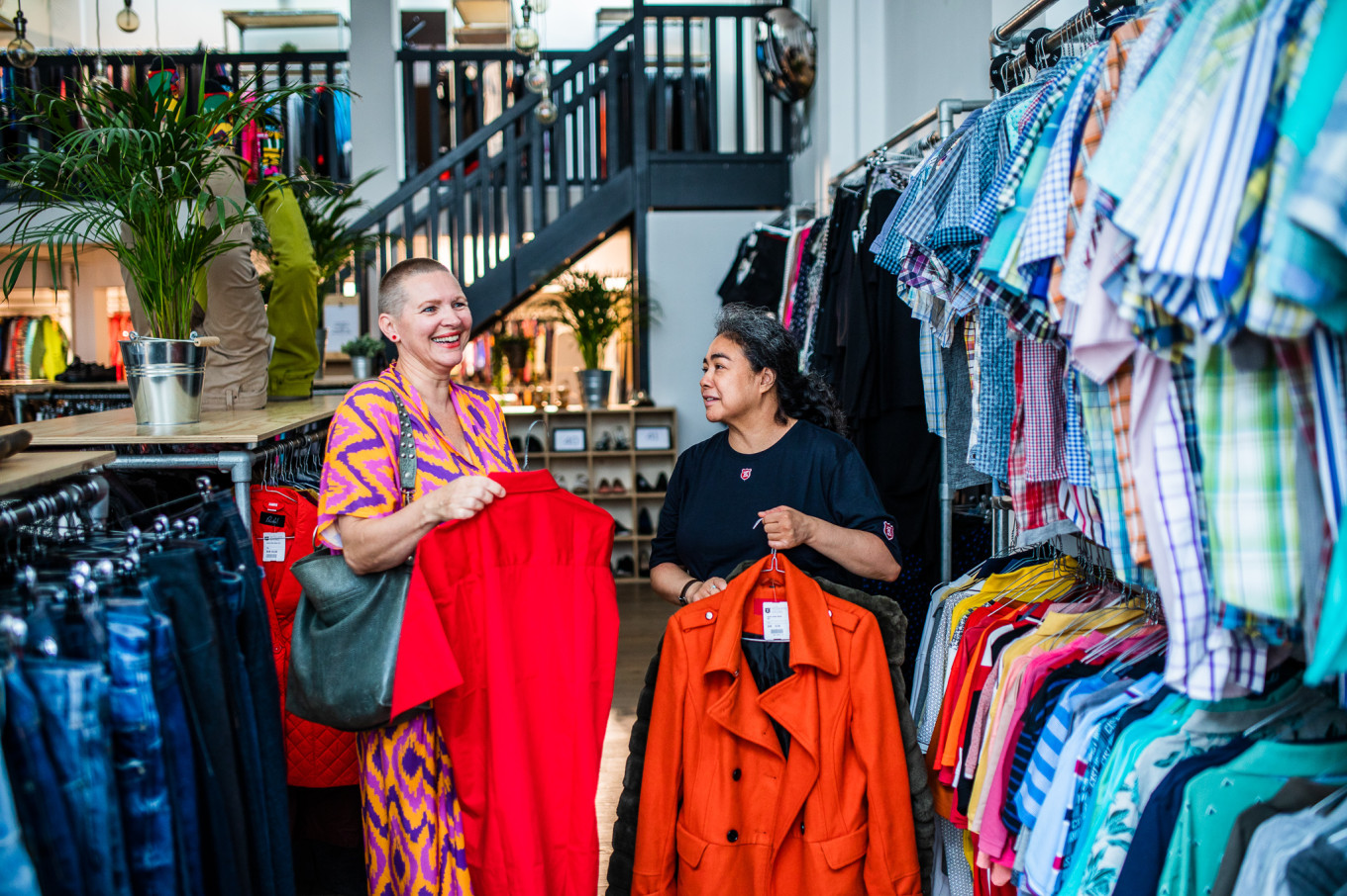 Een medewerkster staat in de ReShare Store tussen de rekken kleding en zoekt samen met een vrouwelijke klant een jasje uit