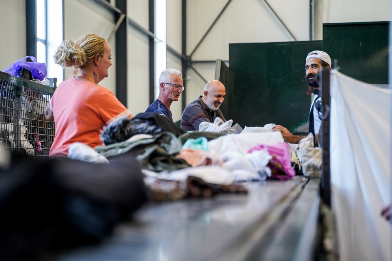 Aan de lopende band staan 3 mannen en een vrouw kleding te sorteren.