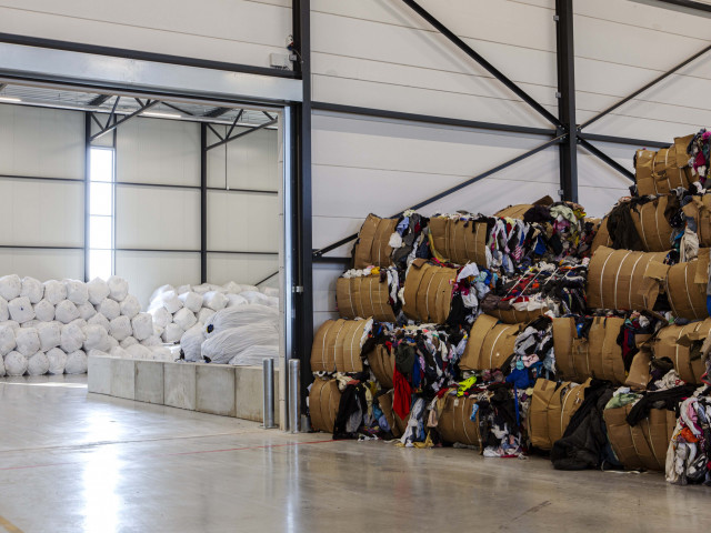 Een grote, licht loods met aan één zijde balen kleding en aan de andere kant grote gevulde witte bigbags