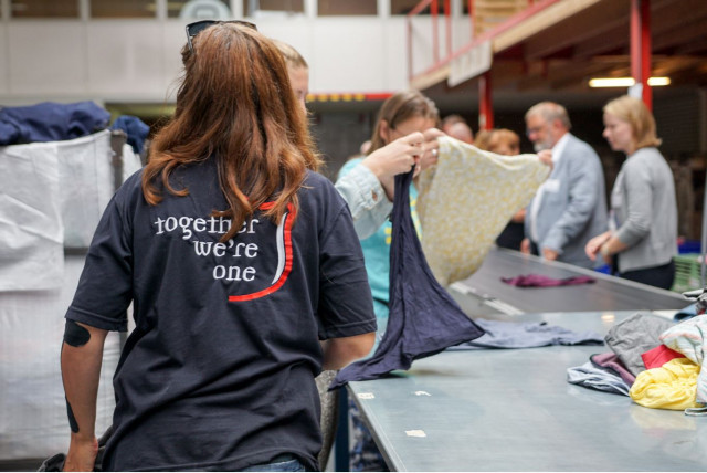 Een sorteermedewerker van ReShare aan het werk met een vest waarop staat "Together we are one"