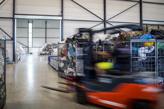 Vanuit een steekwagen wordt uitgekeken op een grote loods voor sortering en opslag van textiel